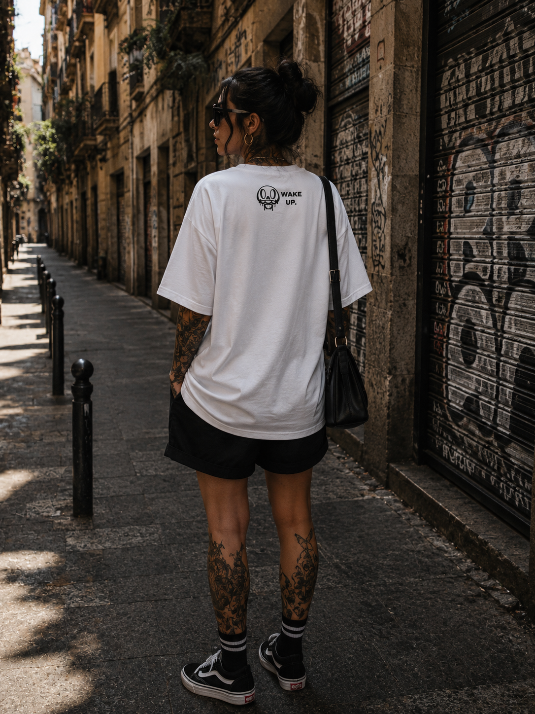 Vista trasera de la camiseta blanca Wake Up con la calavera hip hop en un callejón de Barcelona