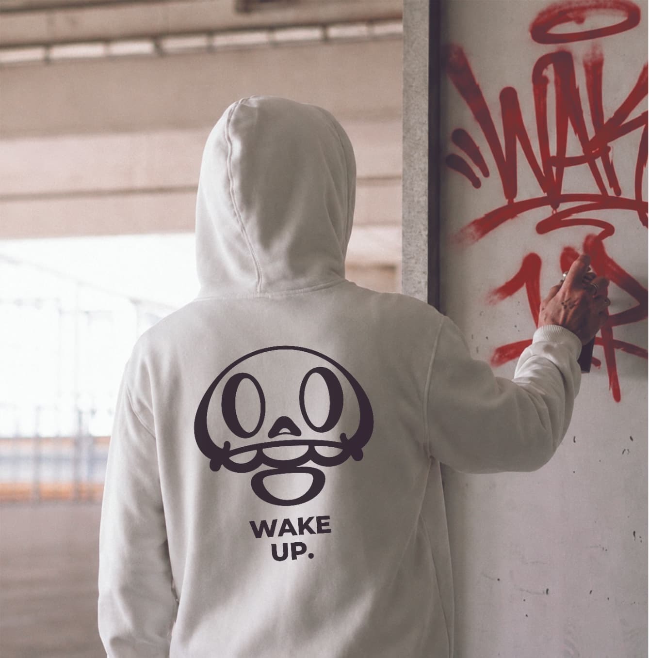 Chico con la sudadera blanca Wake Up pintando un tag en la pared